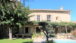 Un edificio con tetto in tegole, una piscina e un giardino curato con diverse piante e una panchina.