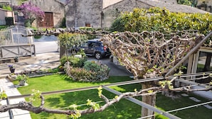 Un giardino con un pergolato, un'auto parcheggiata sullo sfondo e un edificio con facciata in pietra.
