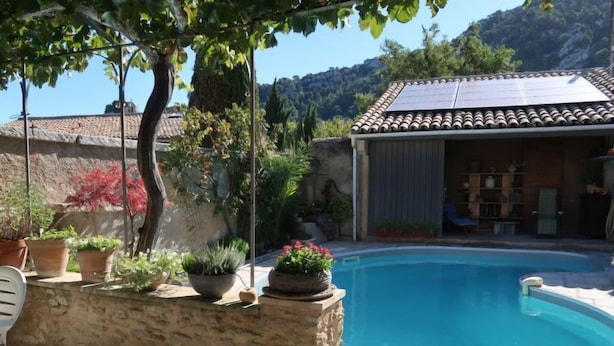 Una piscina con parete in pietra, piante in vaso e pannello solare sul tetto.