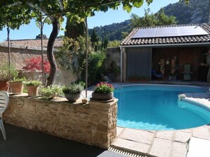 Uma piscina com muro de pedra, plantas em vasos e um painel solar no telhado.