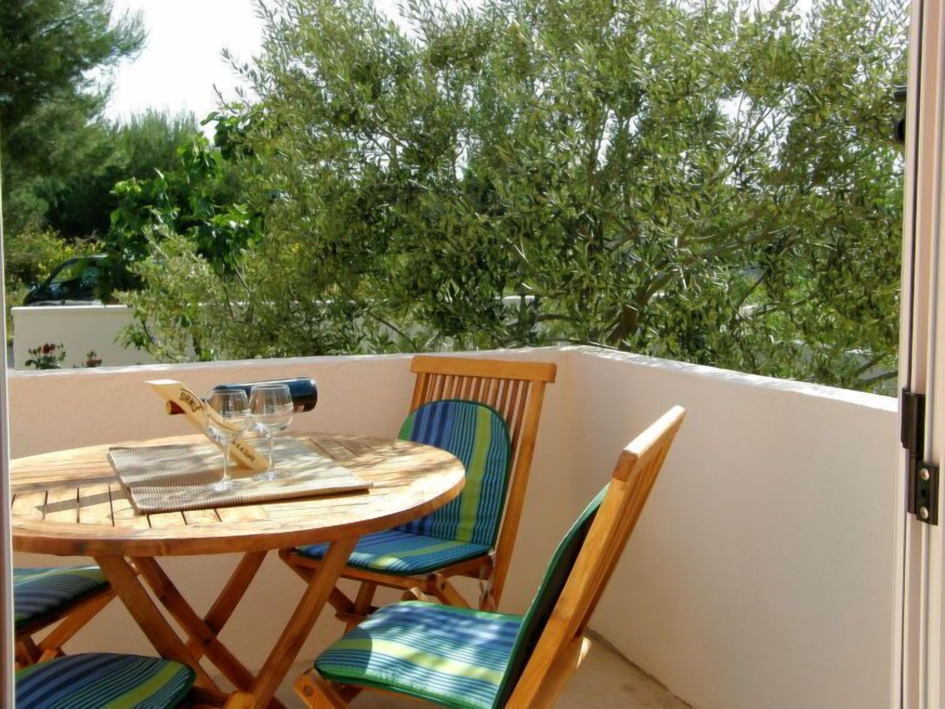 Ein kleiner Balkon mit Sitzgelegenheit im Freien, ausgestattet mit einem runden Holztisch, zwei Stühlen und einem Weinglas.