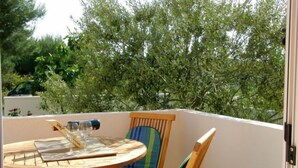 Un pequeño balcón exterior con una mesa redonda de madera, dos sillas y una copa de vino.