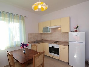 Een kleine keuken met een eettafel, stoelen, een magnetron, oven en een koelkast.