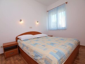 Een slaapkamer met een enkel bed, nachtkastje en een raam met dunne gordijnen.