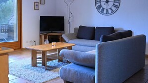 Olohuoneessa on sohva, sohvapöytä, televisio ja suuri seinäkello.