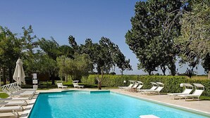 A rectangular swimming pool with clear blue water, surrounded by white lounge chairs and a hedge. - Le Capanne I by Interhome (Grosseto)
