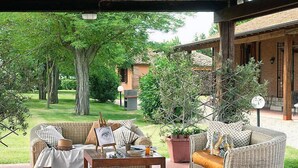 A covered outdoor seating area with wicker furniture, a table, and potted plants. - Le Capanne I by Interhome (Grosseto)