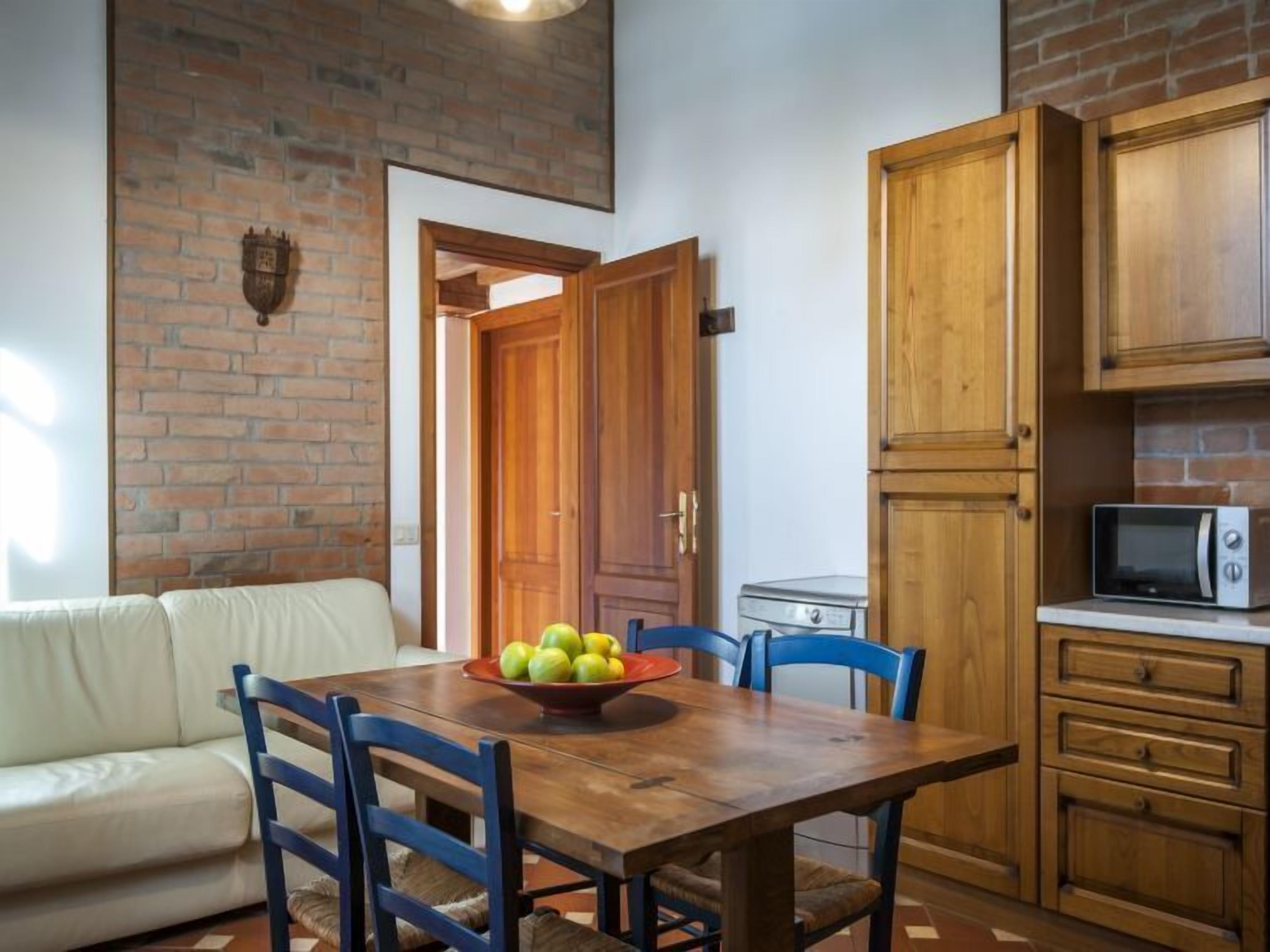 A kitchen with a wooden table, chairs, a microwave, and a brick wall.