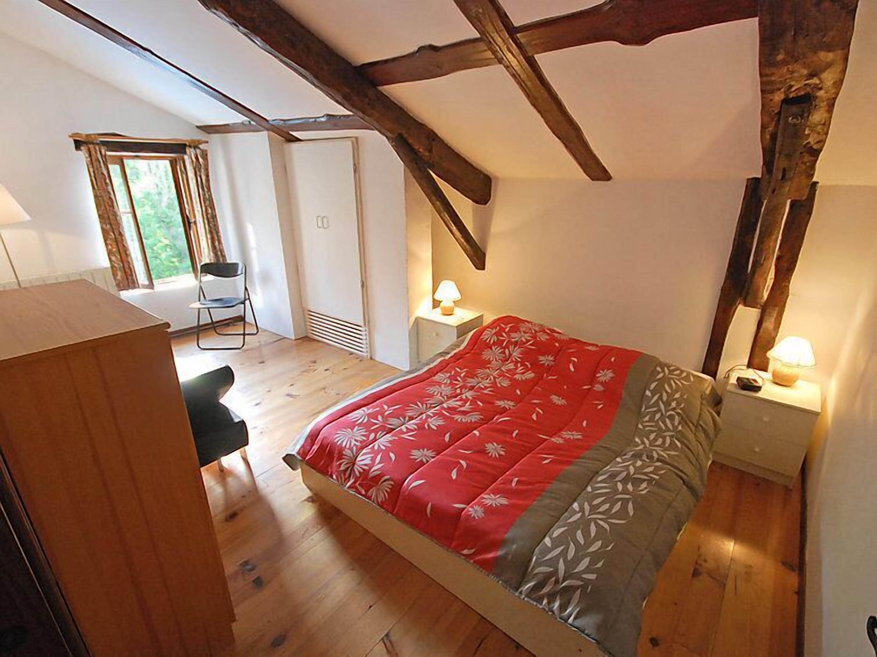 A bedroom with a bed, a desk, a chair, and a nightstand with a lamp.