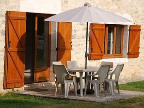 A stone building with wooden shutters, a table with chairs, and a white umbrella.