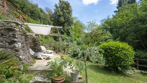 A stone wall with a wooden deck, outdoor seating, and potted plants in a lush garden setting. - Apartment Giallo by Interhome (Loro Ciuffenna)
