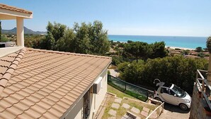 A residential building with a tiled roof overlooking a coastal area with a beach and trees.