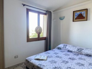 Een slaapkamer met een bed, een raam met gordijnen, een wandlamp en een lijst met een afbeelding.