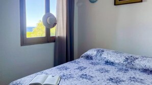A bedroom with a bed, a window with curtains, a wall-mounted light, and a framed picture.