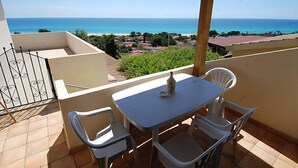 A balcony with a table and chairs, overlooking a coastal view with houses and the sea.