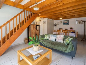 A cozy living room with a wooden staircase, a green sofa, a glass coffee table, and a dining area with a table and chairs. - Brive 1 by Interhome (Vaux Sur Mer)