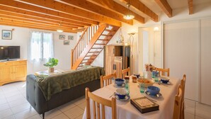 A cozy dining area with a wooden table set for four, surrounded by wooden chairs. A staircase with wooden railings leads to an upper level.
