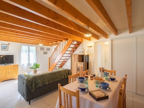 A cozy dining area with a wooden table set for four, surrounded by wooden chairs. A staircase with wooden railings leads to an upper level. - Brive 1 by Interhome (Vaux Sur Mer)
