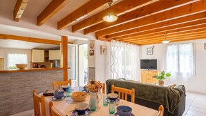 A cozy dining area with a wooden table set for two, a television, and a window with curtains.