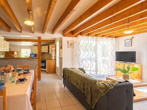 A cozy living room with a sofa, a dining table with chairs, a kitchen area, and a television on a wooden cabinet. - Brive 1 by Interhome (Vaux Sur Mer)