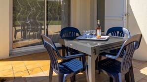 A patio with a table and chairs, a bottle of wine, and a glass set.