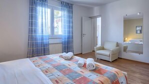 A hotel room with a bed, a chair, a window with curtains, and a mirror on the wall. - Apartment Nika by Interhome (Umag)