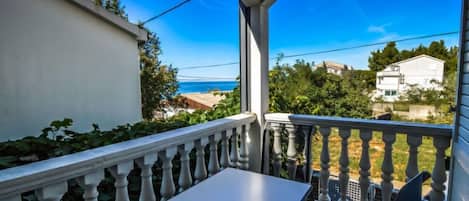 Un balcone con tavolo e sedie, affaccia su una zona costiera con case e vegetazione.