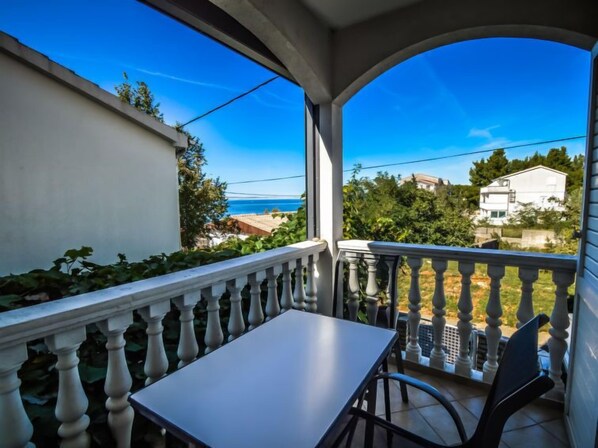 A balcony with a table and chairs, overlooking a coastal area with houses and greenery.