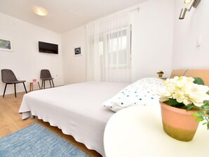 Ett sovrum med en säng, två stolar, ett litet bord, en tv och en krukväxt.