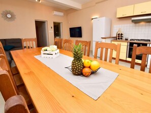 Uma área de refeições com uma mesa de madeira, cadeiras, um jogo americano branco e uma fruteira com abacaxi, laranjas e limões.