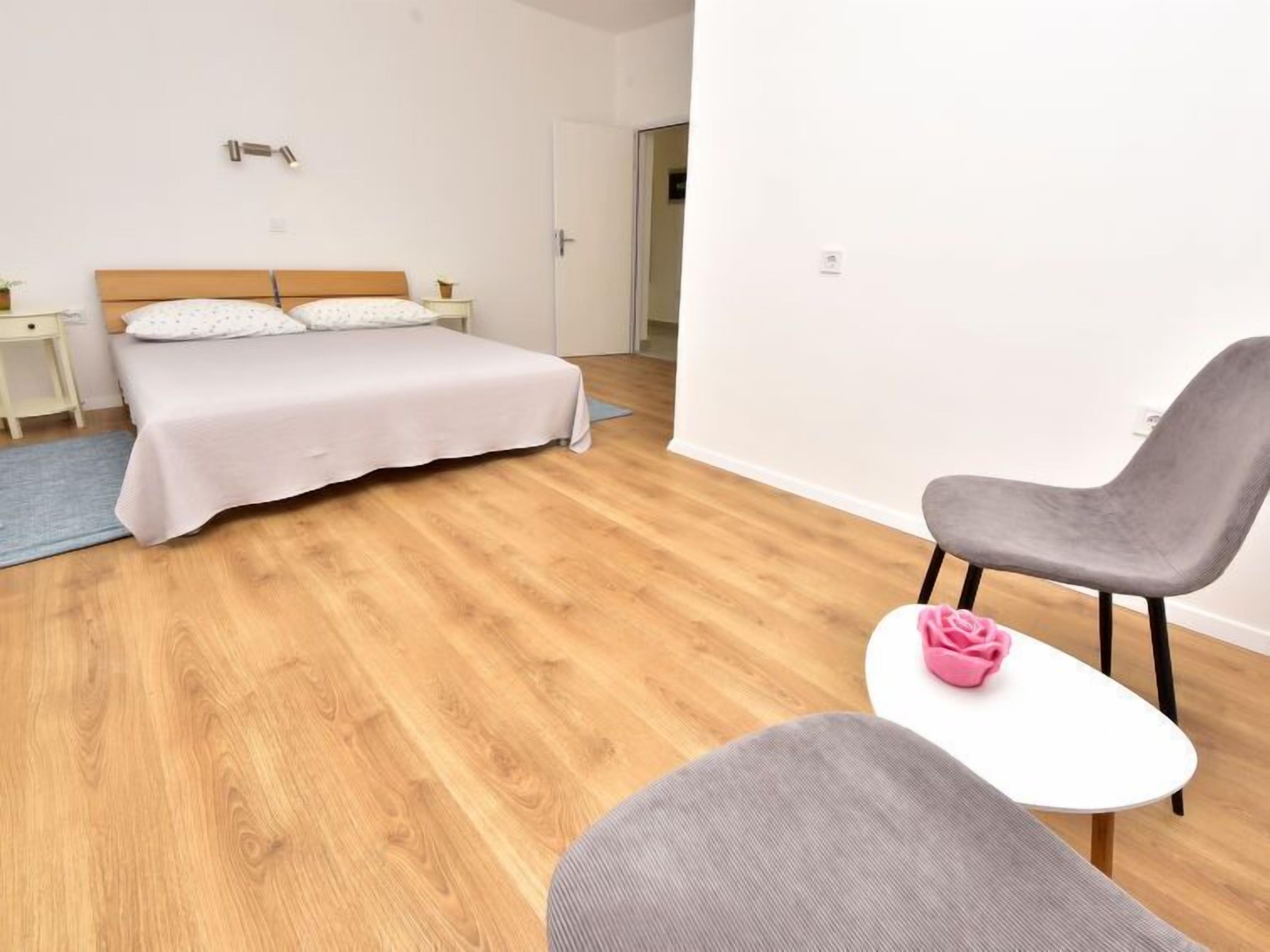 A bedroom with a bed, a chair, a small table, and a nightstand.
