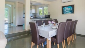 A dining area with a table set for six, surrounded by six chairs. There is a kitchen in the background with white cabinets and a window. - Vacation home Tea by Interhome (Pašman/Nevidane)