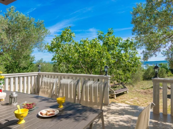 An outdoor dining area with a wooden table, chairs, and a view of the sea.