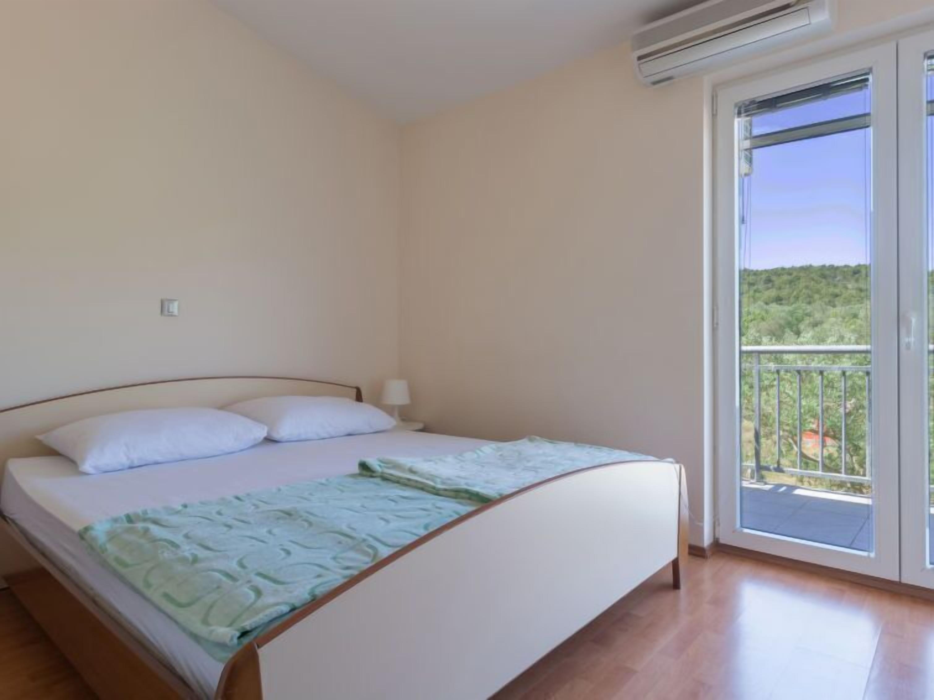 A bedroom with a bed, a nightstand, and a window with a view of greenery.