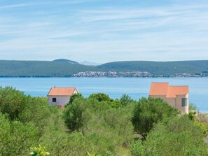 A coastal view with two buildings, one with a red roof and another with a beige roof, surrounded by greenery and a distant town across the water. - Vacation home Tea by Interhome (Pašman/Nevidane)