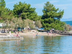 Una zona junto al lago con gente relajándose junto al agua, rodeada de árboles y un muro de piedra.