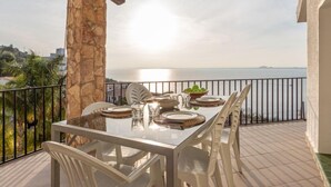 A balcony with a table set for dining, overlooking a body of water and a distant shoreline. - Joan Sarda by Interhome (Roses)