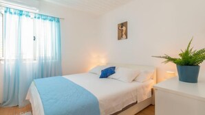 Un dormitorio con cama, una mesita de noche con planta y una ventana con cortinas.