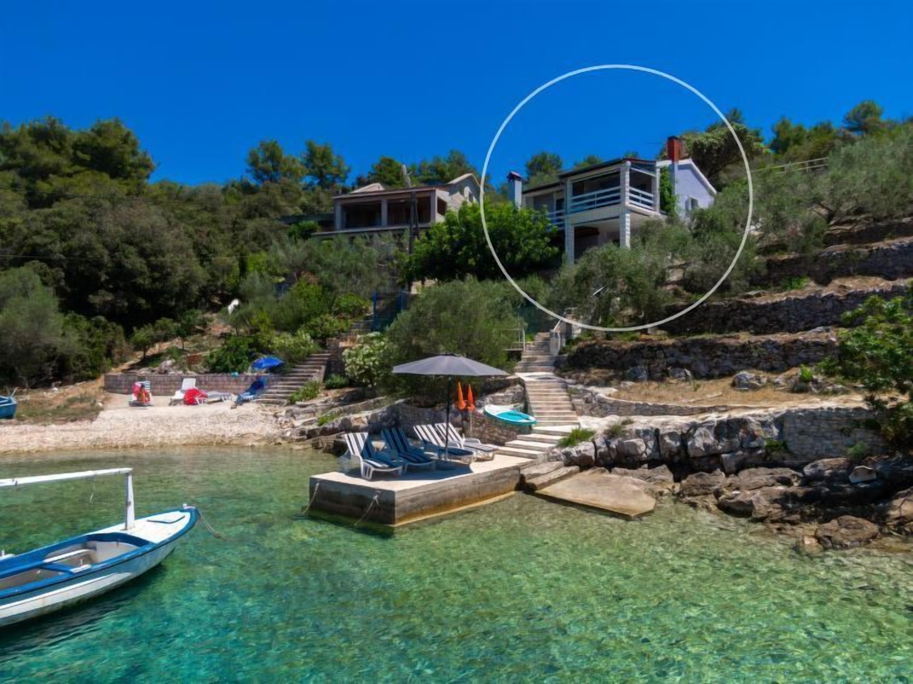 Uma propriedade costeira com vista clara para o mar, um barco atracado na praia e uma escadaria que leva a um edifício.