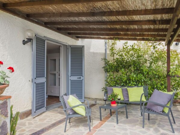 An outdoor patio with a covered area, a seating arrangement, and a door leading to an interior space.