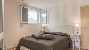 Un dormitorio con cama, dos mesitas de noche, ventana y puerta.
