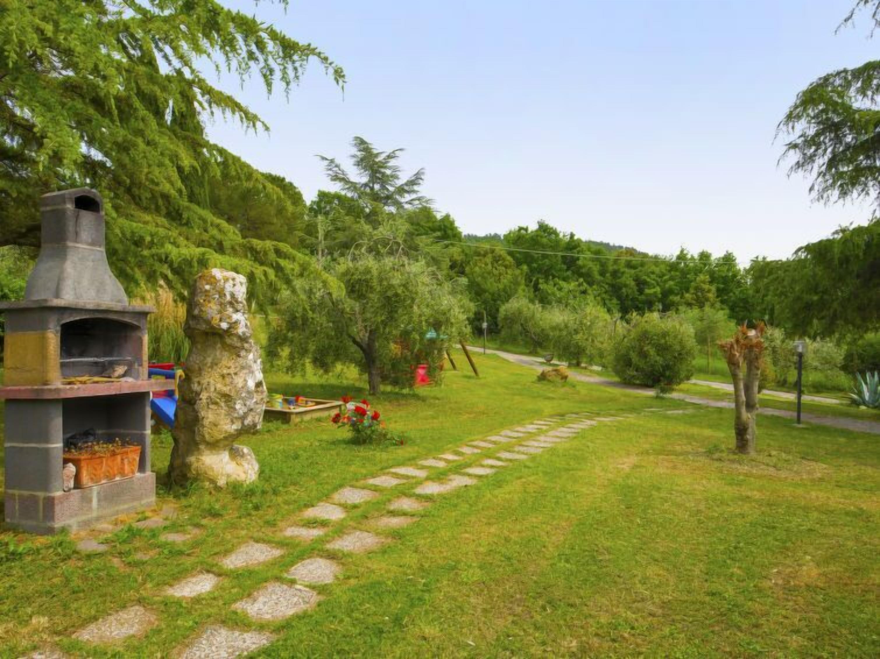 A stone barbecue grill and a stone statue in a lush garden with a stone pathway.