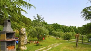 Una parrilla de piedra y una estatua de piedra en un jardín exuberante con un sendero de piedra.