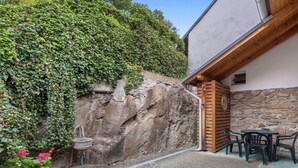 Un patio con un muro de piedra, una pérgola de madera y una mesa con sillas.