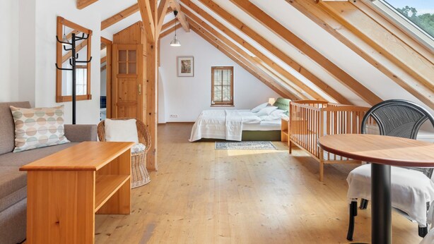 Un dormitorio acogedor en el ático con vigas de madera, una cama, un escritorio y una mesa de comedor.