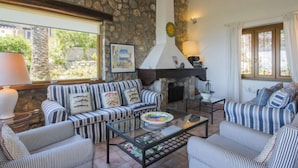 Ein gemütliches Wohnzimmer mit Steinwand, Kamin, gestreiften Sofas und einem Glastisch.