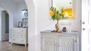 A hallway with a white dresser, a vase with flowers, a clock, and a mirror on the wall. - Delfines by Interhome (Benajarafe)