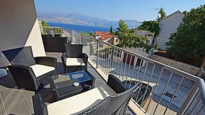Een balkon met rieten meubilair, een glazen tafel en uitzicht op zee en bergen.