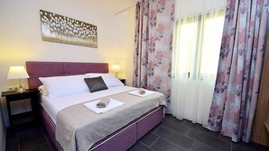 Hotelkamer met een groot bed, twee nachtkastjes, een wanddecoratie en een raam met bloemen gordijnen.