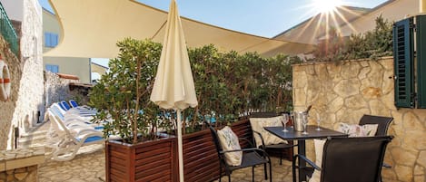 An outdoor seating area with a table and chairs, a sunshade, and a pool in the background.